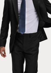 Czarna marynarka o satynowym wykończeniu, biała koszula elegancka i teksturowany niebieski krawat. Posiada dopasowany krój i staranne detale guzików.