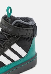 Μ�αύρο και τιρκουάζ μεσαίου ύψους αθλητικό παπούτσι με λευκές ρίγες, υφασμάτινη επιφάνεια, φουντωτό γιακά και μαύρη λωρίδα. Διαθέτει θηλιά σε σχήμα δαχτυλίου σε πράσινο χρώμα.