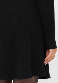 Robe noire à côtes avec des manches longues, tissu texturé, ourlet évasé et ajustée à la taille. Présente une finition lisse et une légère élasticité.
