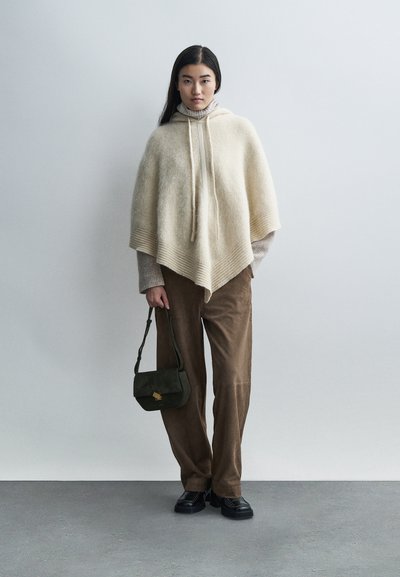 Bézs színű, kapucnis kötött poncsó, bordázott szegéllyel; barna bőszárú kordnadrággal és egy kis sötétzöld kézitáskával párosítva. Fekete cipő.