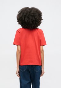 Prosty czerwony bawełniany t-shirt z krótkimi rękawami, okrągłym dekoltem i prostym fasonem, noszony z wysokim stanem niebieskich dżinsów.