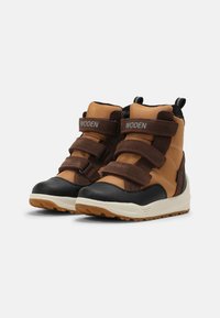 Botas altas castanhas e laranjas com fechos de velcro, biqueira preta e sola de borracha texturizada, apresentando a marca Woden nas alças.