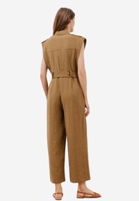 Brun ärmlös jumpsuit med bälte i midjan, design med vida ben och axelkläppar. Tillverkad av strukturerad tyg för en avslappnad passform.