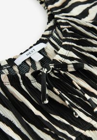 Tissu rayé noir, beige et blanc avec un cordon noué et une étiquette de vêtement blanche "NEXT" cousue dans la couture.