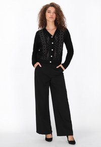 Mustakurras ribbed kardigan V-kauluksella, koristeltu hopea- ja värillisen helmi-kuvioin, yhdistettynä leveälahkeisiin mustiin housuihin ja mustiin korkokenkiin.