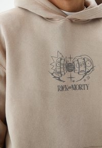 Sweat-shirt beige en matériau doux avec un design imprimé de deux personnages de dessin animé et le texte « RICK AND MORTY » en noir.