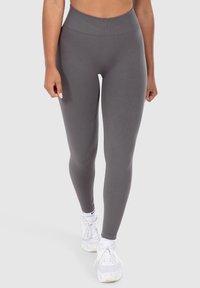 Graue Leggings mit hohem Bund, aus einem glatten, dehnbaren Stoff gefertigt. Kombiniert mit weißen Sportschuhen. Keine Muster oder sichtbaren Nähte.