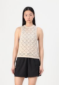 Top smanicato lavorato a maglia beige con un motivo a rombi, dotato di scollatura rotonda e bordo a coste, abbinato a pantaloni corti neri.