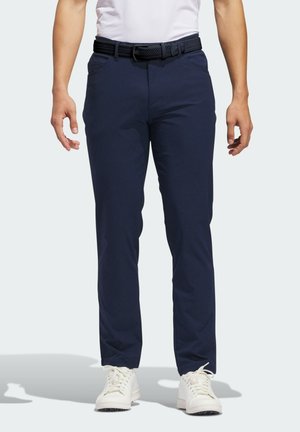 Pantalon bleu marine avec une coupe slim, fabriqué en tissu léger. Comprend des poches avant, une ceinture en toile texturée noire et des baskets blanches.