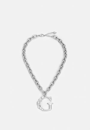 Collier chaîne en argent avec grand pendentif "G" orné de cristaux clairs sur fond blanc.