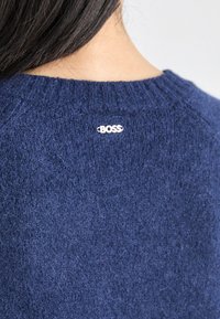 Marine modra pletena majica z teksturirano tkanino, z okroglim izrezom in majhnim belim logotipom "BOSS" na hrbtu.