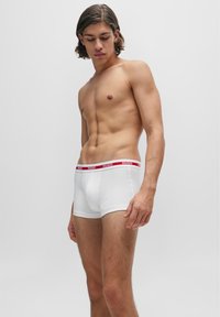 Boxers blancs en coton au design ajusté, avec une bande logo rouge à la taille. Texture lisse, coupe mi-hauteur.
