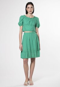 Conjunto verde de dos piezas que presenta una blusa corta con mangas abullonadas y una falda de volantes. La tela tiene patrones cortados y un dobladillo ondulado.