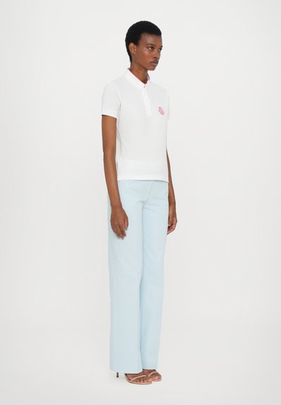 Hvit polo skjorte med korte ermer, rosa krage og brodert logo; paret med lyseblå vide bukser og nude hæler.