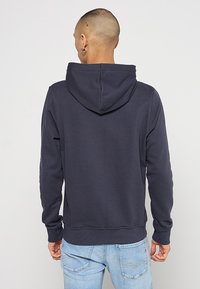 Marineblauwe hoodie met een buidelzak, ribgebreide manchetten en zoom. Bevat een stoftextuur en een capuchon voor extra warmte.
