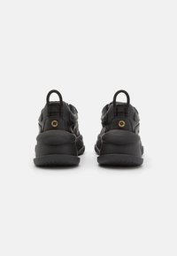 Sneakers neri con un design texture, suola arrotondata e un linguetta sul tallone. Presentano un accento dorato vicino al tallone.