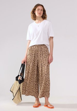 Hvid bomulds T-shirt, løse leopardmønstrede bukser i beige og brune nuancer, sort vævet taske med blomsterdetalje og orange flip-flops.