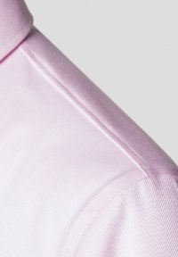Jasnoróżowy kołnierzyk z gładkiego, błyszczącego materiału. Posiada dopasowany krój oraz subtelną strukturalną teksturę na powierzchni.