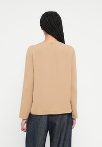 Top bej cu mâneci lungi și decolteu rotund, prevăzut cu un mic fermoar la spate. Material neted, croială lejeră, purtat cu pantaloni din denim închis la culoare.