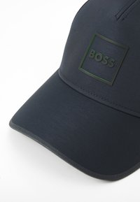 Casquette bleu marine au design élégant, dotée d'une couture en relief, d'une visière plate et d'un logo carré noir bien en vue portant l'inscription "BOSS".
