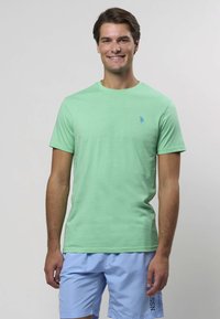 Svetlozelené tričko s krátkym rukávom a okrúhlym výstrihom, s malým modrým logom na ľavej strane hrudníka. Hladká bavlnená tkanina.