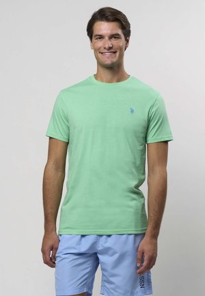 Šviesiai žalia trumpomis rankovėmis medvilninė marškinėliai su apvalia apykakle ir mažyliu mėlynu logotipu kairėje krūtinės pusėje. Lygios medvilnės audinio tekstūra.