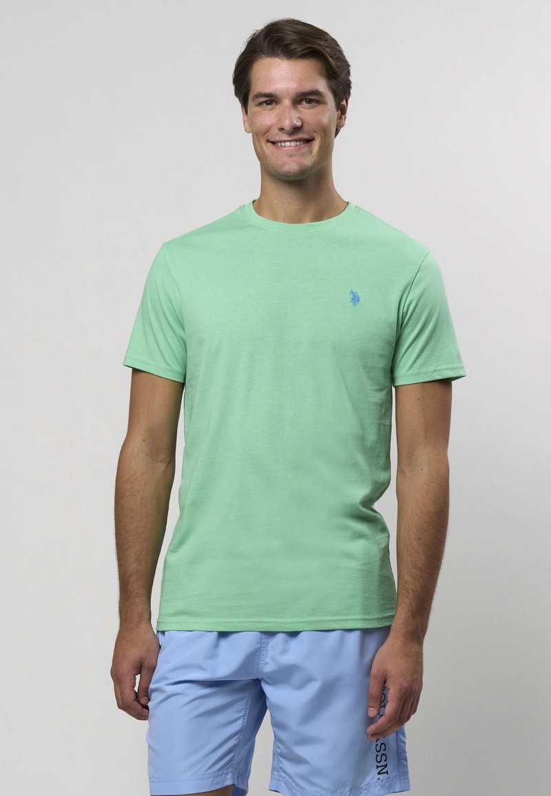 Svetlozelené tričko s krátkym rukávom a okrúhlym výstrihom, s malým modrým logom na ľavej strane hrudníka. Hladká bavlnená tkanina.
