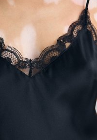 Camisola in satin nera con scollo a V e bordo in pizzo nero, delicato motivo floreale e spalline sottili regolabili.