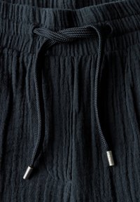 Donkere stof joggers met een gestructureerd oppervlak, voorzien van een elastische tailleband en een koord met metalen punten.