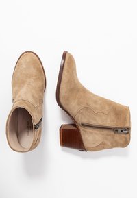 Beżowe zamszowe botki do kostki z wydłużonym noskiem i zakrzywionym designem. Posiadają zamek błyskawiczny z boku oraz podwyższony, drewniany obcas.