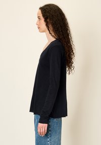 Musta V-kaelusega pikkade varrukatega pehme tekstuuriga ja lõdva lõikega ülaosa. Sobitatud kõrge vöökohaga siniste teksadega, mis loovad vabaaja silueti.