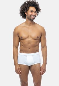 Slip in cotone bianco con texture a coste, fascia elastica in vita e design del pannello anteriore, indossato da un modello su sfondo neutro.
