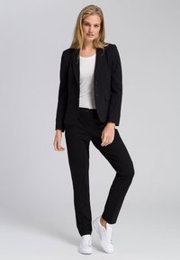 Black tailored blazer and matching trousers, paired with a white top and white sneakers. Smooth fabric, structured design, and slim fit.