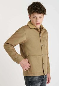 Tanskleurige katoenjack met een corduroy kraag, sluiting met knopen aan de voorkant, twee grote voorzakken en een subtiele textuur.