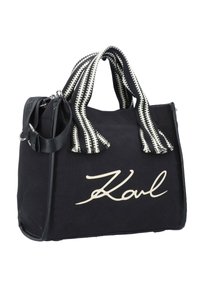 Svart canvas-handväska med vit signatur "Karl"-logotyp, med randiga svarta och vita handtag samt en avtagbar axelrem.