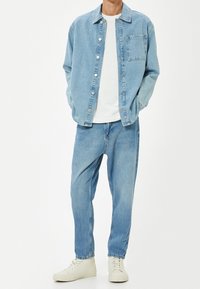 Světle modrá džínová bunda s knoflíkovým zapínáním, v kombinaci s bílým tričkem a světle modrými uvolněnými džíny. Celý outfit doplňují bílé tenisky.