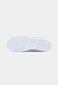 Witte rubberen zool met een gestructureerd grippatroon en cirkelvormige accenten, met het "LACOSTE"-logo in een subtiele uitvoering.