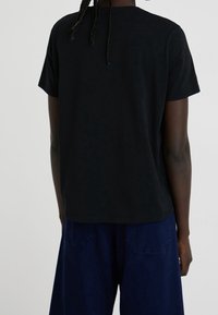 Svart bomulls-T-shirt med avslappnad passform och korta ärmar, med en enkel design och mjuk textur. Synliga sömmar längs fållen.