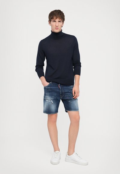 Marinefarbener Rollkragenpullover und verwaschene Denim-Shorts mit faded Blue-Waschung. Weiße Sneakers runden den lässigen Look ab.