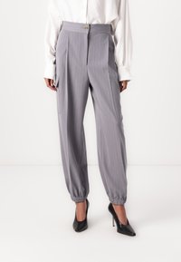 Pantalon gris à rayures avec une taille haute, fermeture à bouton à l'avant et poignets élastiqués ; associé à des chaussures à talons hauts noires.