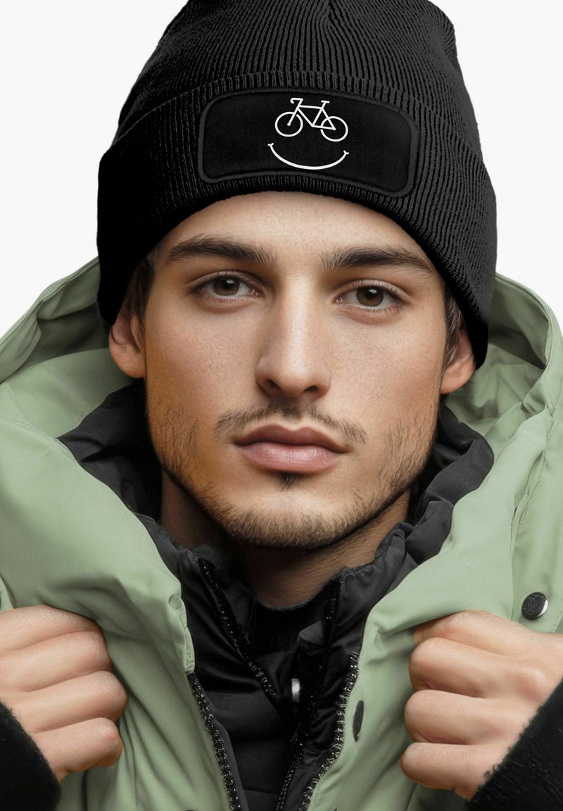Black ribbed beanie with a bicycle and smile graphic; paired with a green puffer jacket over a black zip-up layer.