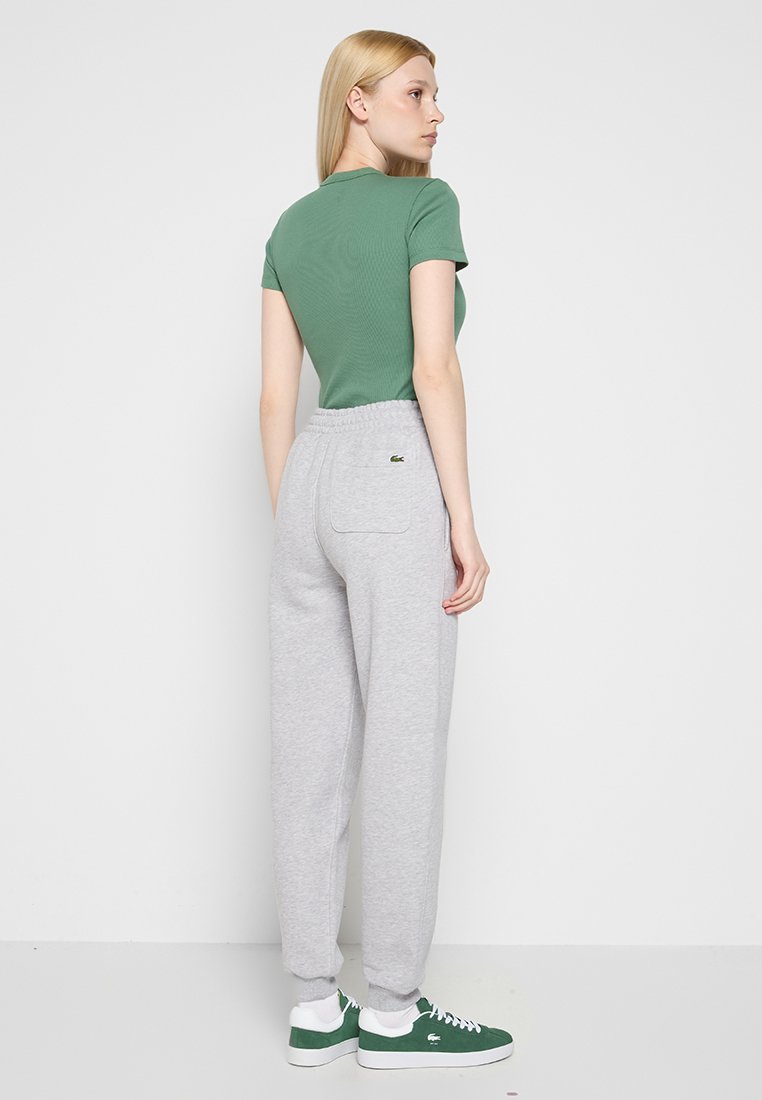Zielona t-shirt w prążki, szare dresy z elastycznym paskiem w talii, boczne kieszenie, logo Lacoste na tylnej kieszeni, zestawione z zielonymi trampkami.