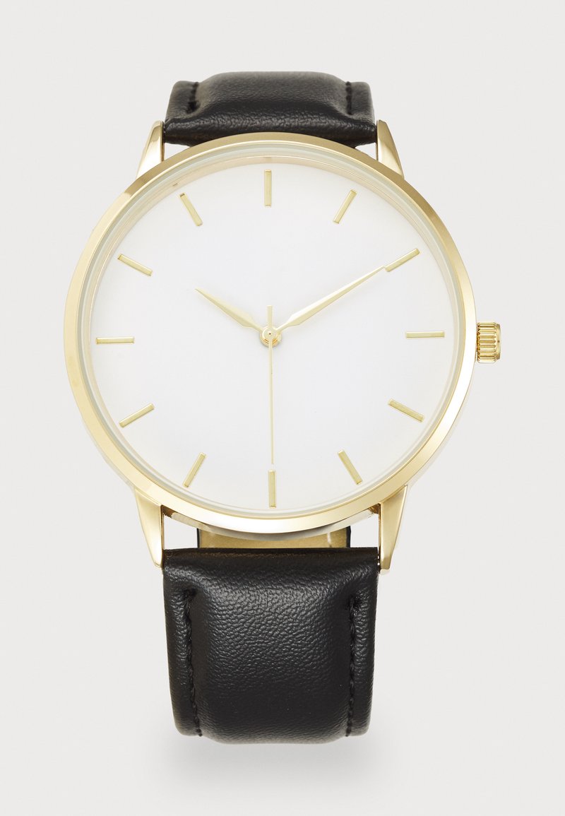Montre dorée avec un grand cadran blanc, bracelet en cuir noir, marqueurs d'heure minimalistes et aiguilles dorées. Conçue avec une forme ronde classique.