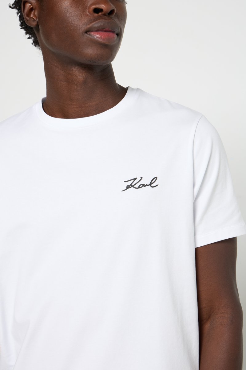 Camiseta de algodón blanca con cuello redondo y mangas cortas, con un pequeño logo bordado en negro "Karl" en el lado izquierdo del pecho.