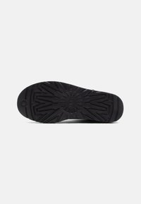 Suela de zapato negra con una superficie de goma texturizada que presenta un patrón de relieve geométrico y un diseño circular central para mejorar la tracción.