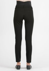 Schwarze, eng anliegende Hose mit hohem Bund, glatter Textur, schlankem Schnitt und zwei Gesäßtaschen. Kombiniert mit flachen, schwarzen Schuhen.