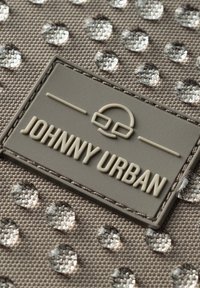 Tessuto grigio testurizzato con puntini argentati in rilievo e lucidi, con un'etichetta del logo grigio ben visibile che recita "JOHNNY URBAN" nella parte inferiore.