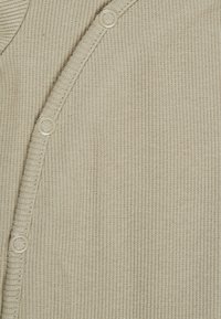 Nahaufnahme von beigem strukturiertem Strickstoff mit einer Reihe runder Knöpfe entlang des Randes, die die Textur und die Knopfdetails hervorhebt.