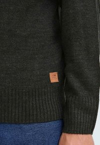 Mørkegrå strikket genser med ribbet tekstur, med et lærmerke på kanten og brukt med blå denim.