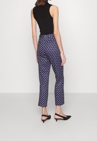 Pantalones con estampado naval en azul marino y líneas finas en blanco y amarillo, con corte recto y cinturilla de altura media, combinados con tacones negros tipo slingback.